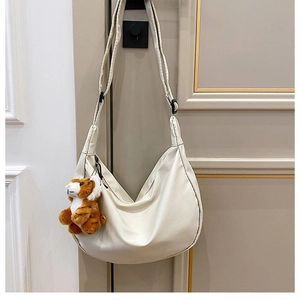 Close-up of cream crescent bag with a cute tiger plush keychain and adjustable strap