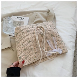 Détail d'un sac en paille tissé avec broderie florale et nœud en dentelle blanche