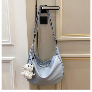 Detail of light blue nylon crescent bag with adjustable strap and plush tiger charm