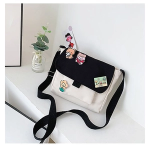 Détail du sac bandoulière en toile avec rabat noir et jolies broches de dessin animé