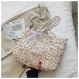 Détail d'un sac cabas en paille avec broderie florale, nœud en dentelle et fermoir aimanté