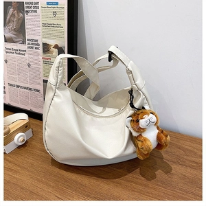 Detail of a beige nylon crescent bag with smooth texture and orange tiger plush charm