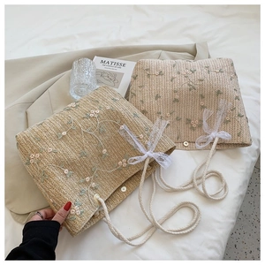 Détails des motifs floraux brodés sur sac en paille tressée avec ruban en dentelle