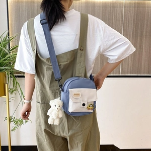 Rear view of model wearing a blue and white nylon crossbody bag with plush bear charm