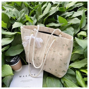 Détail du sac en paille avec broderie florale et nœud en dentelle blanche