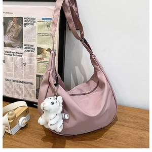 Pink nylon crescent crossbody bag with tiger plush charm on a wooden table detail