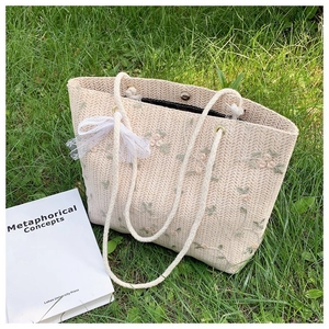 Détail du sac cabas en paille beige avec broderie florale et nœud en dentelle sur herbe