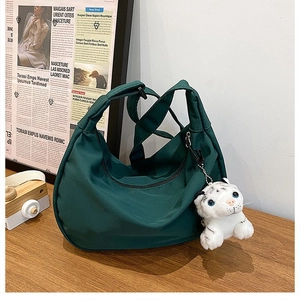 Detail of dark green nylon crescent bag with a cute white tiger plush pendant on a table