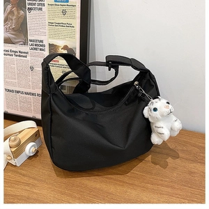 Close-up of black nylon crescent bag on wooden desk with cute white tiger plush pendant