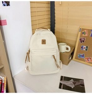 Detailed close-up of cream canvas backpack with brown leather logo and zipper ribbon