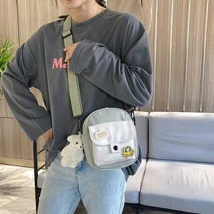 Detail view of mini green canvas crossbody bag with cute cartoon patch and bear charm