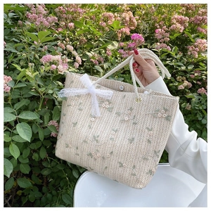 Gros plan détaillé d'un sac en paille avec broderie florale et nœud en dentelle blanche