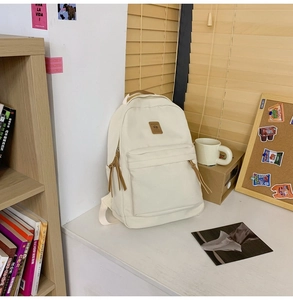 Close-up of white canvas backpack with brown leather logo patch and zip puller detail