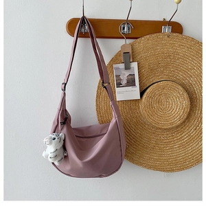 Detail view of purple nylon crescent bag with adjustable strap and small plush charm on a hook