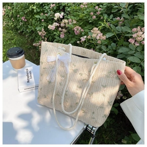 Détail de fleurs brodées, nœud en dentelle blanche et anses en corde sur un sac en paille