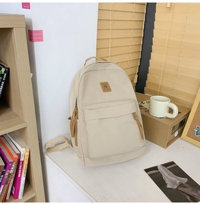 Detail view of cream nylon backpack featuring leather logo patch in a cozy home setting