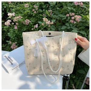 Détail du sac cabas en paille avec broderies florales et nœud en dentelle blanche