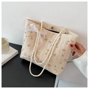 Détail de broderie florale et nœud en dentelle blanche sur un sac fourre-tout en paille