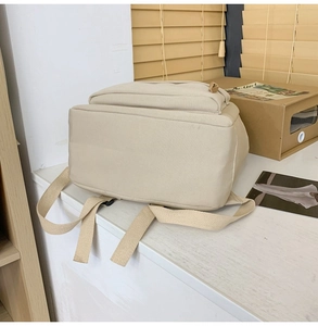 Detailed side view of a beige nylon backpack featuring adjustable straps on wooden background
