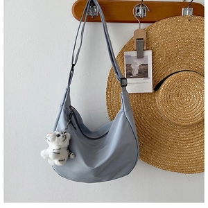 Close-up of light blue nylon crescent bag with cute tiger plush charm on wooden hook