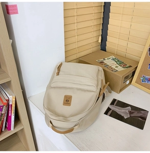 Detail view of a beige nylon backpack with brown leather trim and MR.MI brand logo label