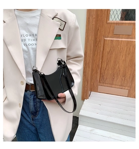 Close-up of black glossy patent leather shoulder bag with silver hardware on a model