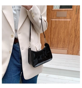 Detailed view of a black glossy patent leather shoulder bag with metallic buckle and slim strap