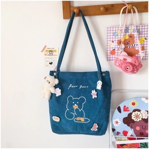 Détail d'un cabas en velours côtelé bleu avec broderie ours et pendentif en peluche