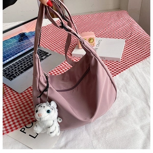 Detail of a dusty pink nylon crescent bag with a cute plush tiger charm on a desk