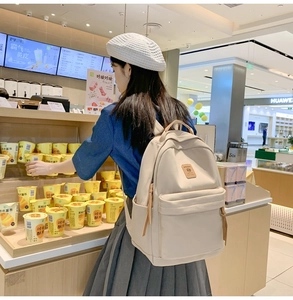 Back view of a minimalist beige nylon school backpack worn by a girl in a bright store