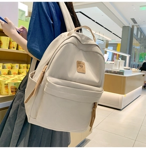 Detailed side view of beige canvas backpack with brown leather logo on a model