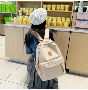 Detail of minimalist beige nylon backpack with brown leather handle and side pocket