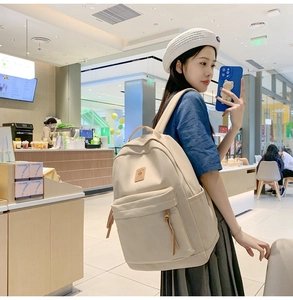 Asian female model wearing a minimalist beige nylon backpack in a stylish cafe setting