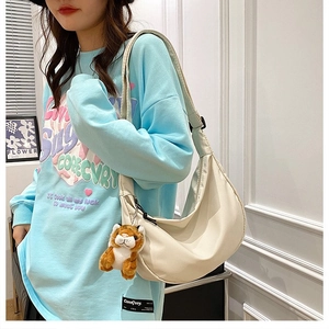 Detail of a beige nylon crescent bag featuring a cute tiger plush charm on the shoulder strap