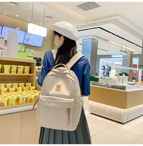 Detail view of the beige nylon backpack showing front pocket and side storage compartment