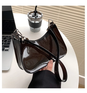 Detailed close-up of glossy black crescent bag with silver hardware on a desk