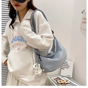Detail of light blue nylon crescent bag with a cute white tiger plush pendant accessory