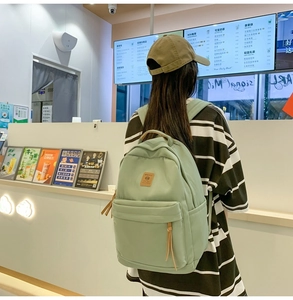 Detail of light green nylon backpack featuring a leather logo patch and zip puller