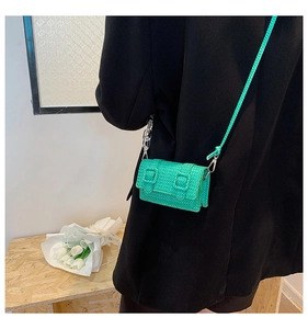 Détail du mini sac tissé vert avec chaîne acrylique porté sur une veste de blazer noire