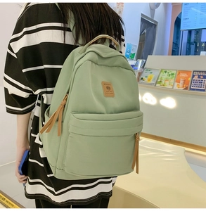 Detailed back view of a light green nylon backpack with a brown leather logo patch