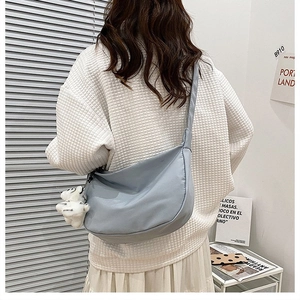 Detail of light blue nylon hobo bag with cute white teddy bear charm and wide shoulder strap