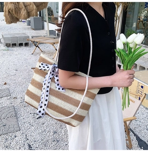 Detail of straw tote bag with brown stripes, polka dot ribbon, and rope handles