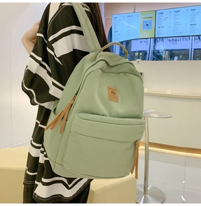 Close-up of minimalist light green nylon backpack featuring a brown leather logo patch