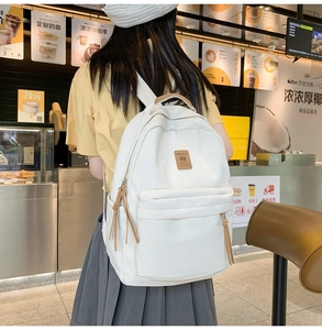 Side view of a beige canvas backpack with brown leather zipper pulls and logo patch
