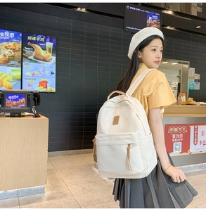 White canvas backpack with leather logo patch detail worn by model in casual setting