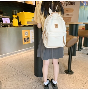 Detail of white nylon backpack featuring large front pocket and brown leather label accents
