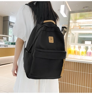Close-up of black nylon backpack featuring leather handle and logo patch in casual setting