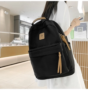 Detail of minimalist black nylon backpack with brown leather logo and top handle on model
