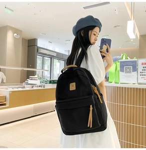 Close-up of minimalist black canvas backpack with brown leather handle and zipper detail