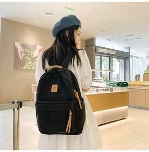 Minimalist black nylon backpack with brown leather trim shown on a model in a cafe